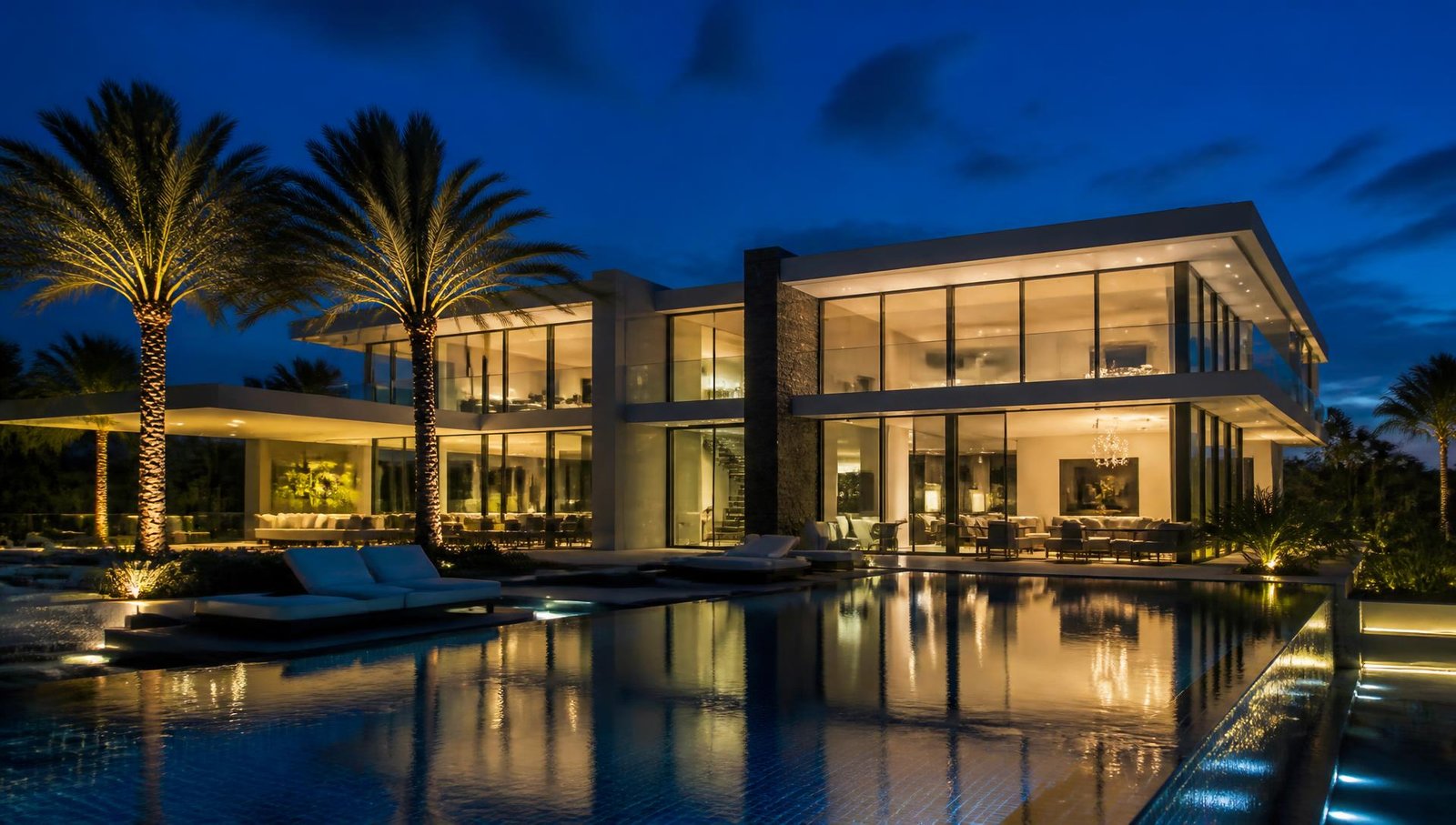Modern Florida home lit at dusk with palm trees and a reflecting pool